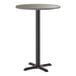 A round bar height table with a reversible gray and white laminated top and a black cast iron base.