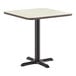 A square standard height table with a reversible white birch or ash laminated top and a black cast iron base.