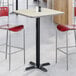 A square bar height table with a reversible gray and white laminated top and a black cast iron base.