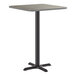 A square bar height table with a reversible gray and white laminated top and a black cast iron base.