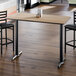 A rectangular bar height table with a reversible white birch and ash laminated top and a black cast iron base.