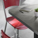 A square bar height table with a reversible gray and white laminated top and a black cast iron base, shown with red chairs.