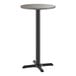 A round bar height table with a reversible gray and white laminated top and a black cast iron base.