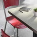 A rectangular laminated table with a light wood finish, paired with red metal chairs and a small potted plant on top.