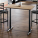A rectangular bar height table with a reversible white birch and ash laminated top and a black cast iron base.