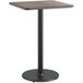 A Lancaster Table & Seating bar height table with a black base and reversible wood top.