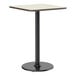 A square bar height table with a reversible white birch or ash laminated top and a black cast iron pedestal base.