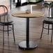 A round, standard height table with a reversible white birch and ash laminated top and a black cast iron base.