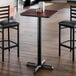 A square bar height table with a reversible cherry and black laminated top and a black cast iron base.