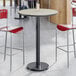 A round bar height table with a reversible gray and white laminated top and a black cast iron base.