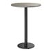 A round bar height table with a reversible gray and white laminated top and a black cast iron base.