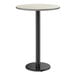 A round bar height table with a reversible gray and white laminated top and a black cast iron base.