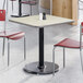A square reversible gray and white laminated table with a black cast iron base, surrounded by red chairs in a dining area.