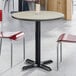 A round, standard height table with a reversible gray and white laminated top and a black cast iron base.