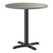 A round, standard height table with a reversible gray and white laminated top and a black cast iron base.