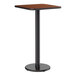 A square bar height table with a reversible walnut and oak laminated top and a black cast iron base.