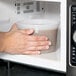 A hand holding a ChoiceHD plastic deli container of food in a microwave.