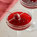 A glass of red liquid with a Les Vergers Boiron Black Cherry puree cocktail with a cherry on top.