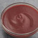 A bowl of Les Vergers Boiron Dark Red Plum fruit puree on a gray surface.