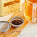 A strainer with Twinings Earl Grey tea leaves over a glass of tea.