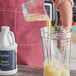 A person pouring Capora Banana Fruit Smoothie Mix into a blender.