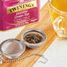 A strainer full of Twinings Jasmine Green loose leaves over a cup of orange liquid.