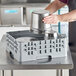 A man using a Cambro soft gray plastic rack to hold metal containers on a counter.
