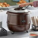 A woman using an Avantco copper soup kettle to serve soup at an outdoor event.