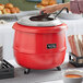 A woman holding a silver lid over a red Avantco soup kettle.