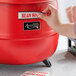 A person's hand putting a sticker on a red Avantco soup kettle.