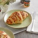 A plate with a Schulstad almond filled croissant and a knife on a table with more croissants and a cup of tea.