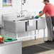 A man washing dishes in a Regency three compartment commercial sink.