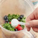 A hand using a spoon to add white powder to a blender.