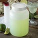 A white Carlisle Store 'N Pour container with a silver cap next to a glass of margarita.