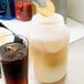 A person using a Carlisle Store 'N Pour container to pour a lemon wedge into a jar of liquid.