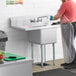 A man in an apron washing a Regency stainless steel commercial sink.