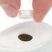A hand holding a CAC bone white saucer with a plastic container with a white cap