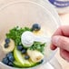 A hand holding a spoon with white powder over a blender.