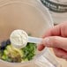A hand holding a measuring spoon with white powder in it.