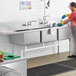 A man wearing gloves washing dishes in a Regency stainless steel three compartment sink.