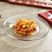 An Anchor Hocking glass plate with a dish of pasta and cheese on a table.