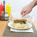 A hand holding a Carlisle clear plastic lid over a plate of food.