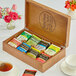 A Bigelow wooden tea chest open to reveal 8 compartments filled with assorted tea bags.