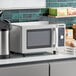 A Solwave stainless steel commercial microwave on a counter with a coffee maker and other items.