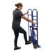 A woman pushing a blue Vestil appliance hand truck.
