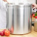 A person holding a Vollrath Wear-Ever Classic Select Heavy Duty Aluminum Stock Pot with a wooden spoon in it.
