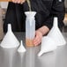 A person pouring liquid into a white Tablecraft funnel.