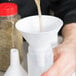 A person pouring liquid into a white Tablecraft plastic funnel.