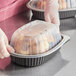 A person in gloves holding a D&W Fine Pack black plastic container with food and a dome lid.