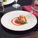 A person's hand holding a fork over an Arcoroc glass dinner plate with pasta.